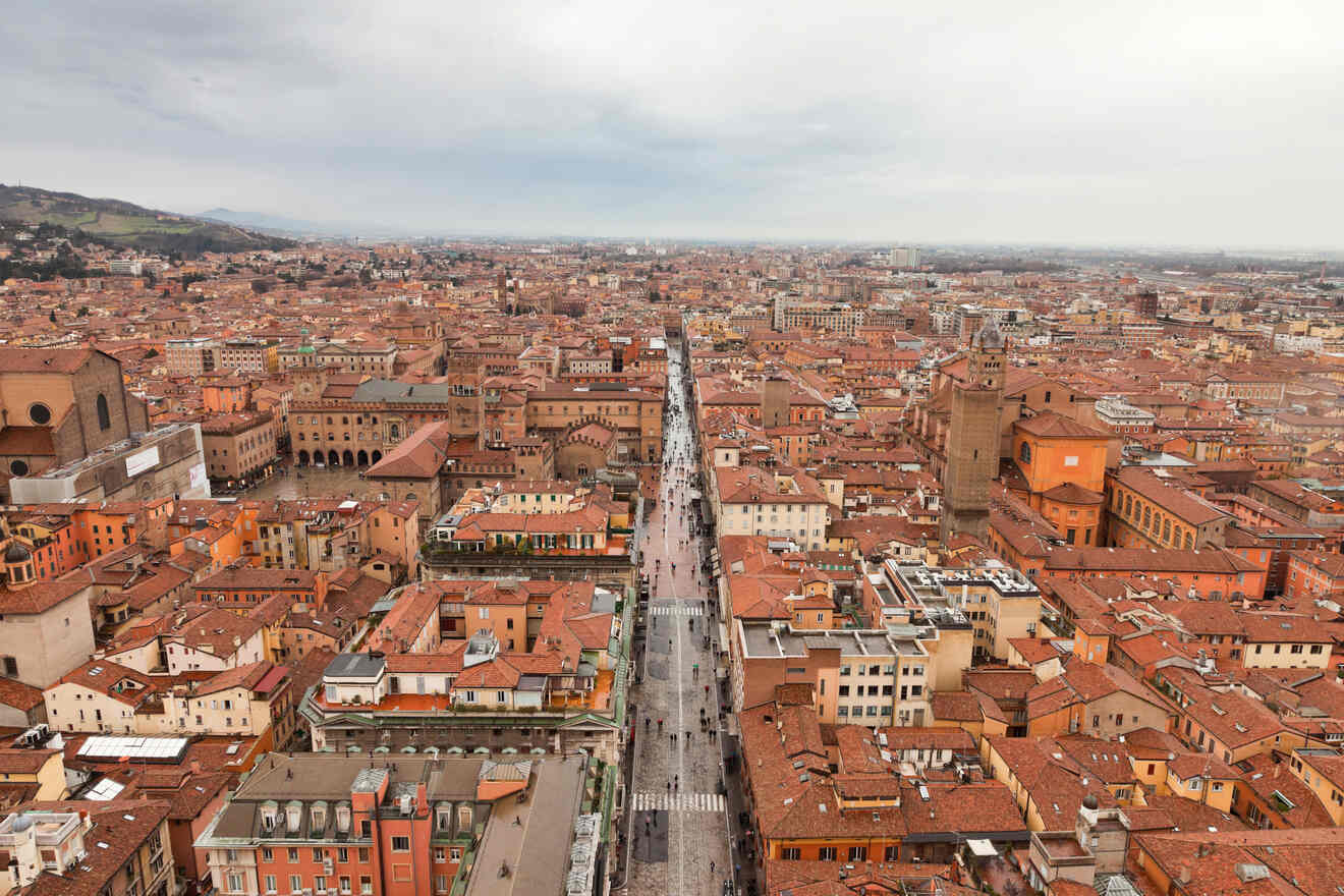 Broad aerial perspective of Bologna's cityscape, showcasing the dense urban layout, historic architecture, and the distant rolling hills.
