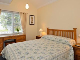 Cozy bedroom with a double bed covered in a floral quilt, a desk, and a window allowing natural light in.