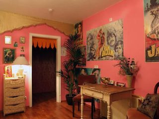 A quirky and colorful vintage room decorated with pink walls, retro movie posters, and a cozy seating area.