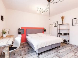 A minimalist bedroom with a large double bed, a simple white and gray color scheme, a small dining area, and modern décor.