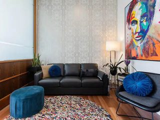 An artistic living room with a bold, colorful portrait on the wall, a dark grey sofa, and a unique multicolored rug