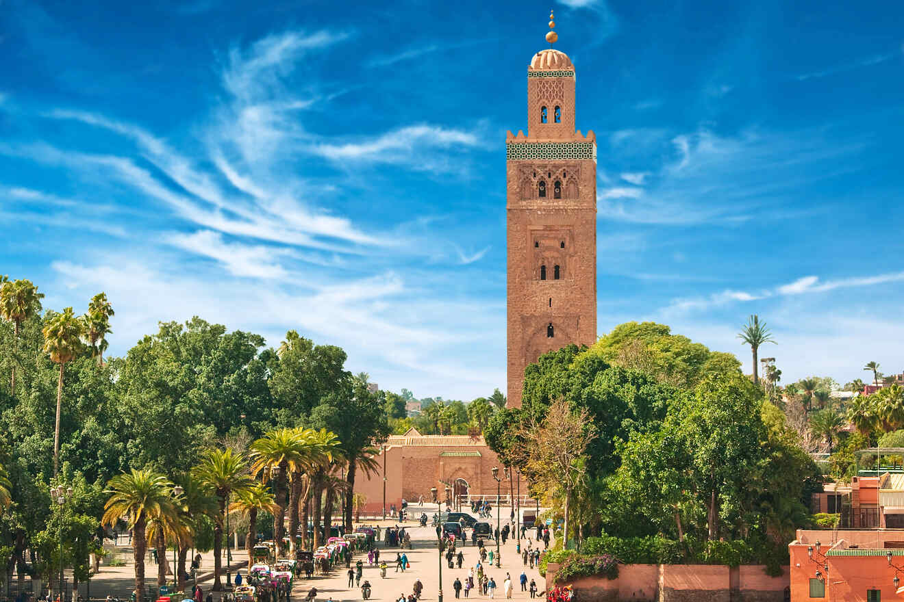 Iconic Koutoubia Mosque towering over Marrakech amidst lush greenery and palm trees on a sunny day with blue skies