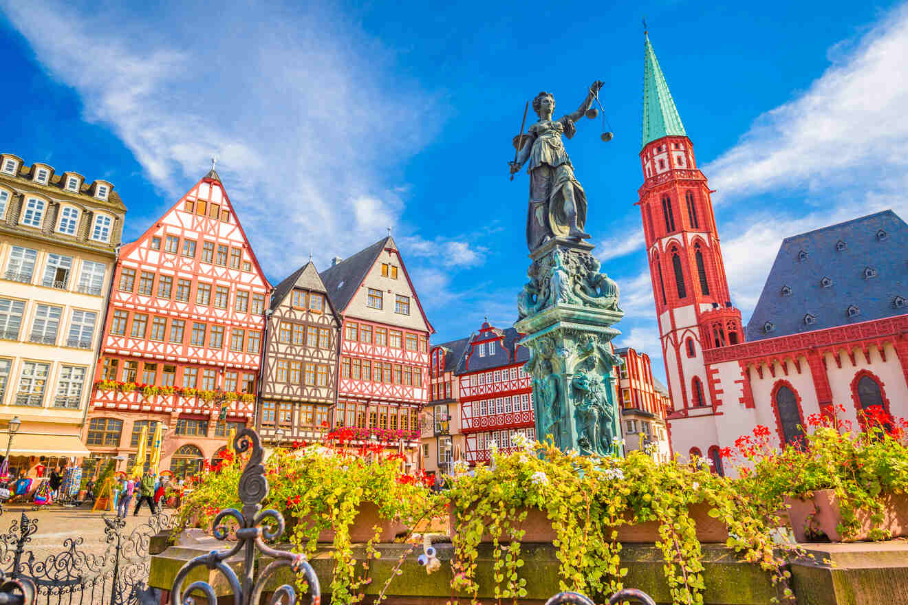 Historic Römerberg square in Frankfurt, Germany, showcasing half-timbered houses, the Justice Statue, and the Old St. Nicholas Church against a blue sky