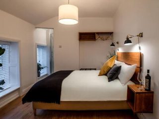 Modern minimalist bedroom with a large bed, black and tan bedding, wooden headboard, and an en suite bathroom.