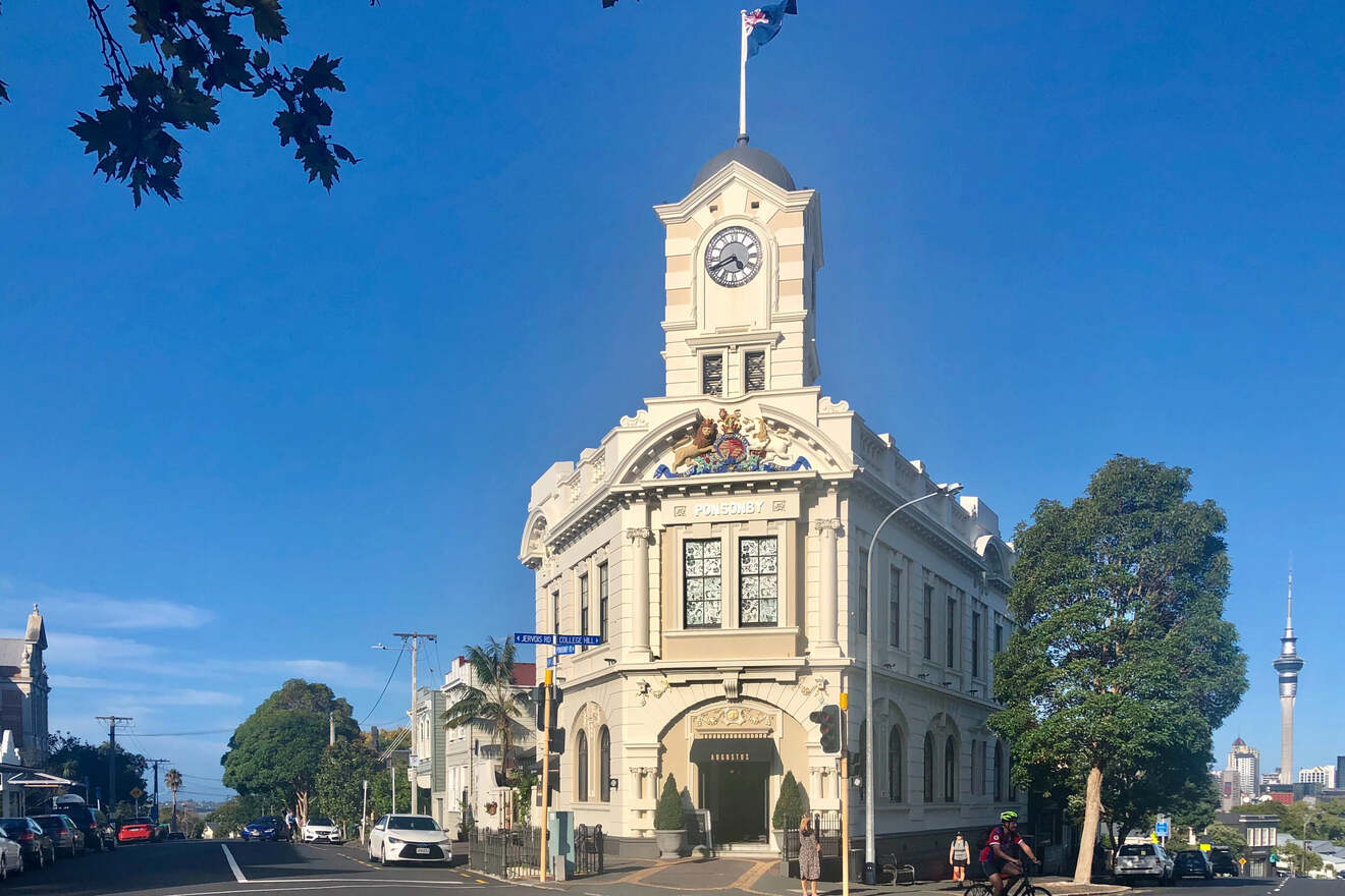 A historic building with ornate architectural details and a clock tower, set against a clear blue sky with the Sky Tower visible in the background