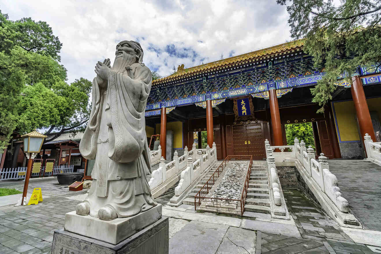 A statue of Confucius standing in front of an ornate building at the Confucius Temple in Beijing.