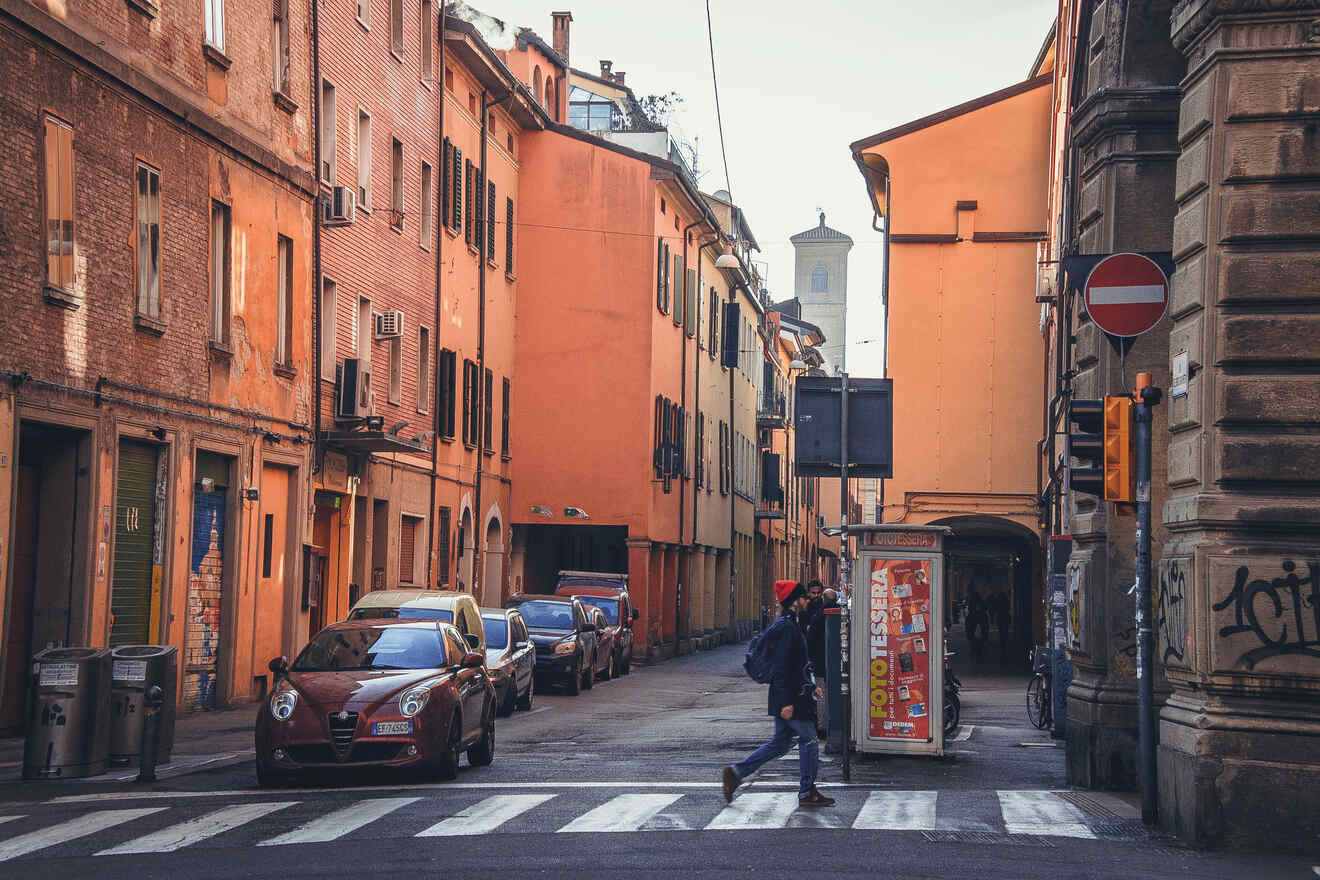 A pedestrian crossing a zebra crossing on a quiet street in Bologna, lined with historic buildings in the warm light of a setting sun.
