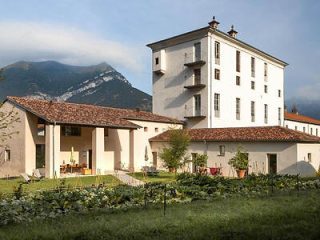 A serene farmhouse surrounded by a lush garden with a mountain backdrop, showcasing rural Italian architecture and tranquil scenery.