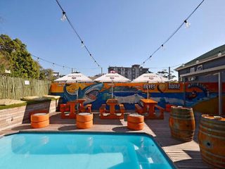 Relaxed outdoor pool area with mural, string lights, orange seating, and umbrellas