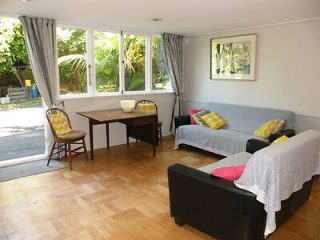 A spacious living room with a wooden floor, featuring two sofas adorned with yellow cushions, a small dining table, and large windows