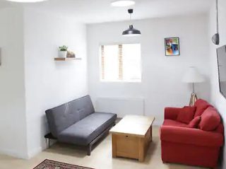 Compact living room with a gray sofa, red armchair, wooden coffee table, and a small red sofa against white walls.