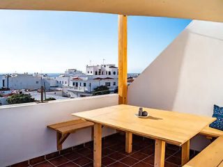 "Simple balcony with wooden table and view of white buildings.