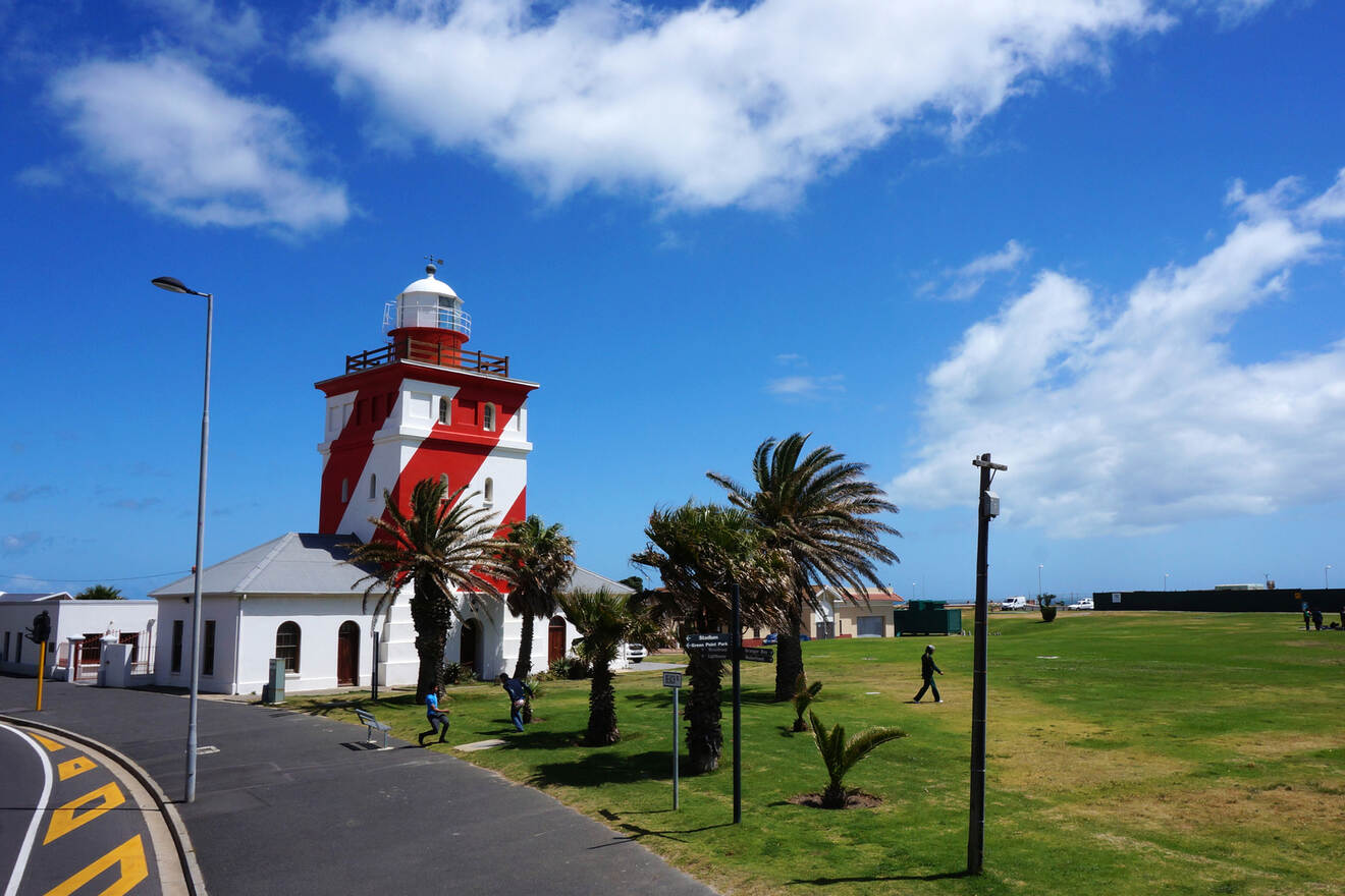 Iconic red and white lighthouse surrounded by palm trees and a lush green lawn under a partly cloudy sky.