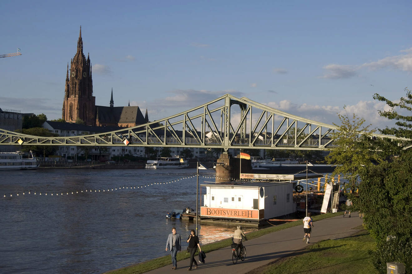 Evening scene by the Main River with the Eiserner Steg bridge, pedestrians, and the Gothic Revival Frankfurt Cathedral in the background