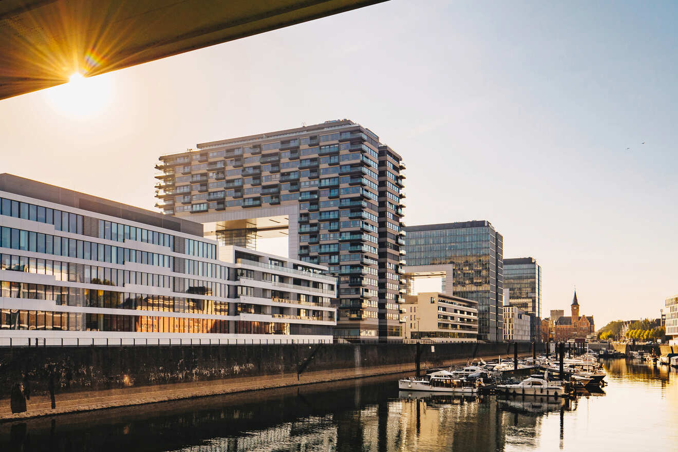 The modern harborfront of Cologne during sunset, with contemporary buildings and docked boats along the calm waters.