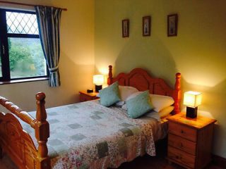 A warm, inviting bedroom with a wooden bed frame, quilted coverlet, and soft lighting from table lamps by the window.