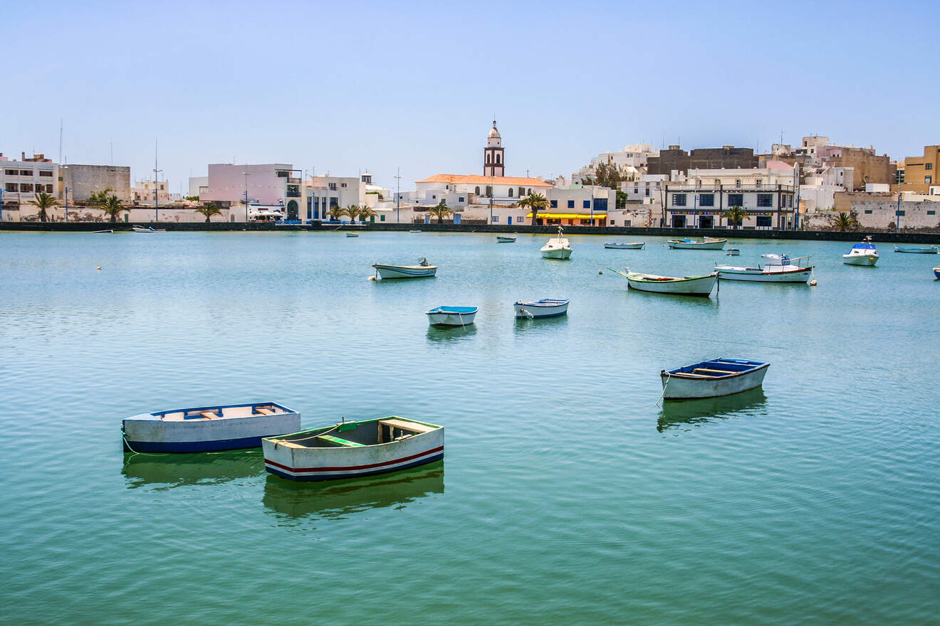 Calm harbor with traditional boats floating on the water, with white-washed buildings and a church in the background in Lanzarote