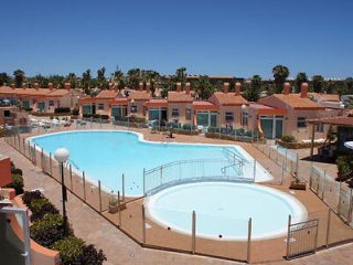 Residential pool area with two large pools and red-roofed houses.