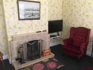 A cozy living room with a red armchair, a fireplace, and a vintage London cityscape print on the wall.