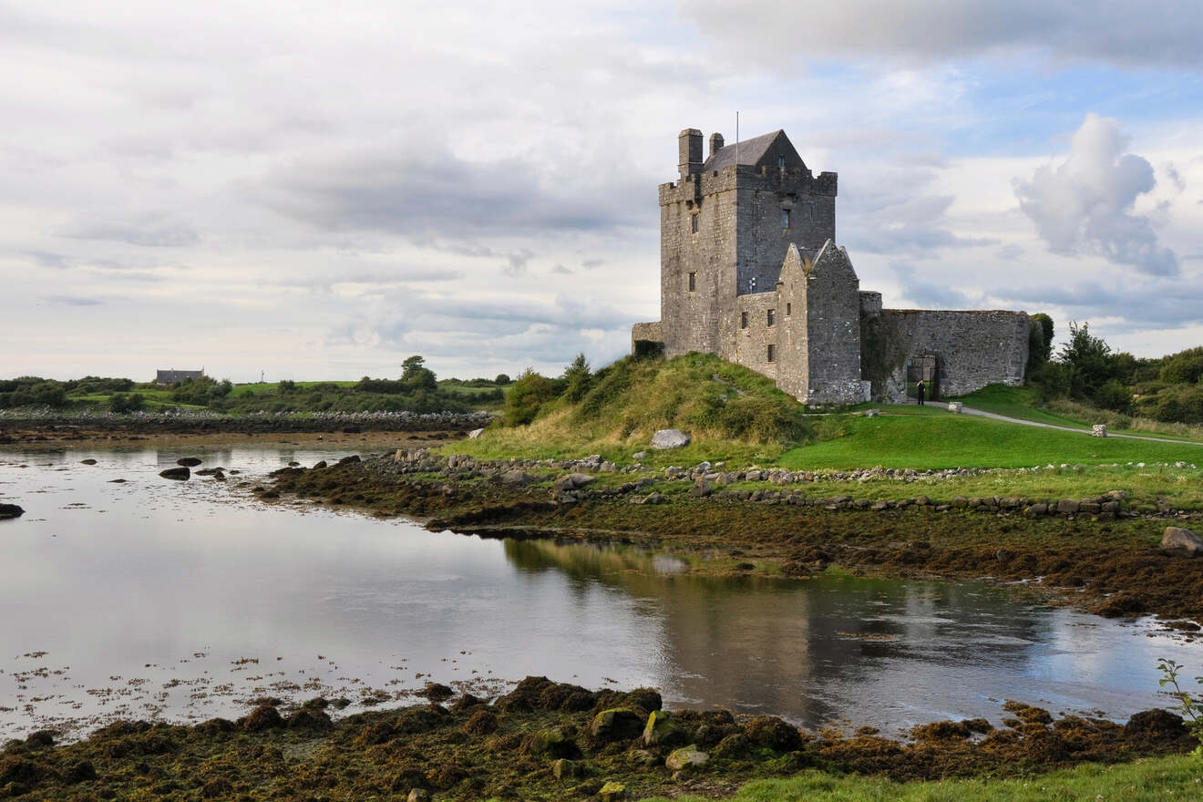 Ancient stone castle on a grassy hill surrounded by water at low tide, with cloudy skies reflecting in the water.