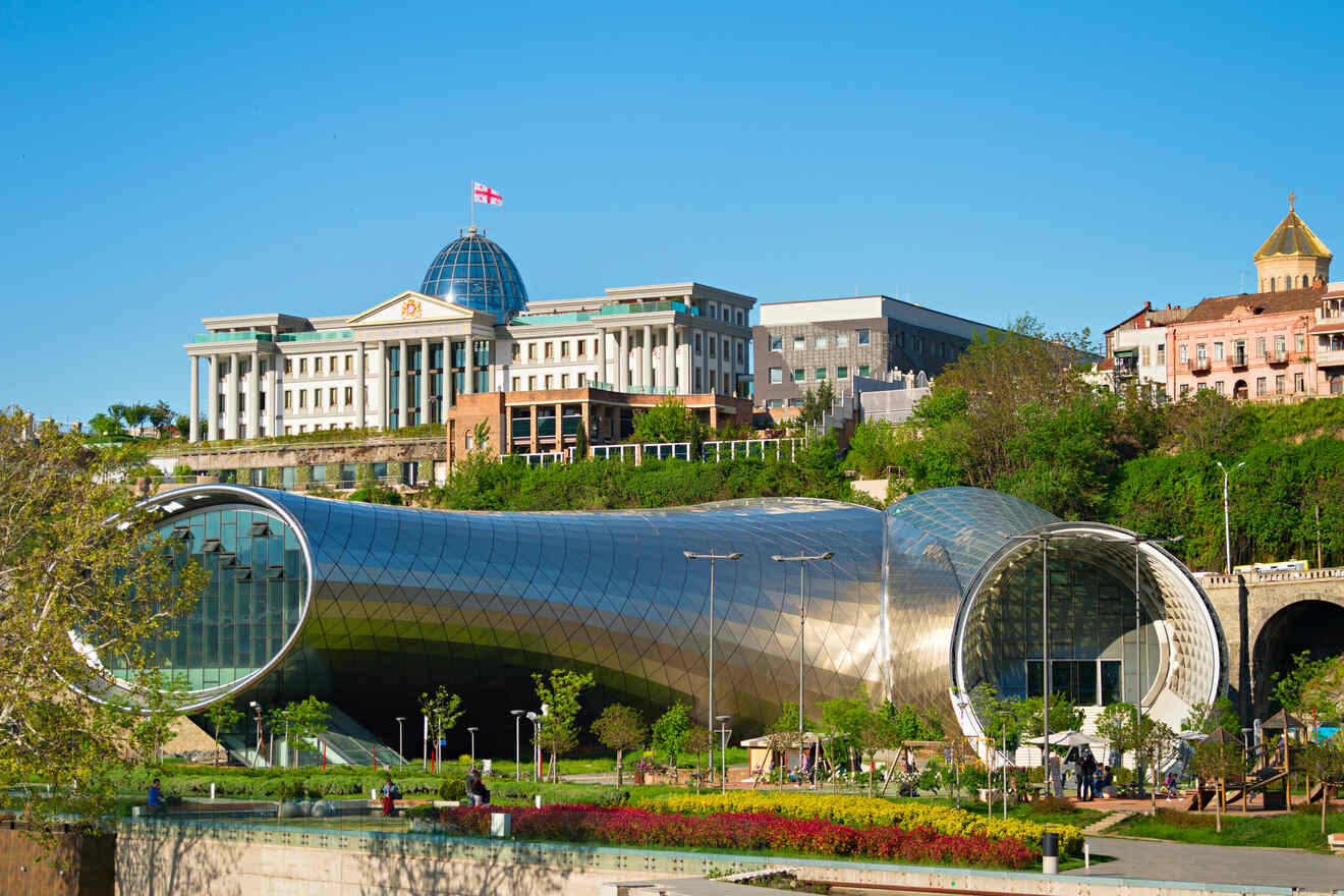 A view of Rike Park and the Presidential Palace in Tbilisi, showcasing modern architecture with the futuristic Rike Concert Hall and the flag of Georgia flying atop the government building