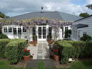 Charming white heritage studio with wisteria draped over the entrance and potted red flowers leading to the front door