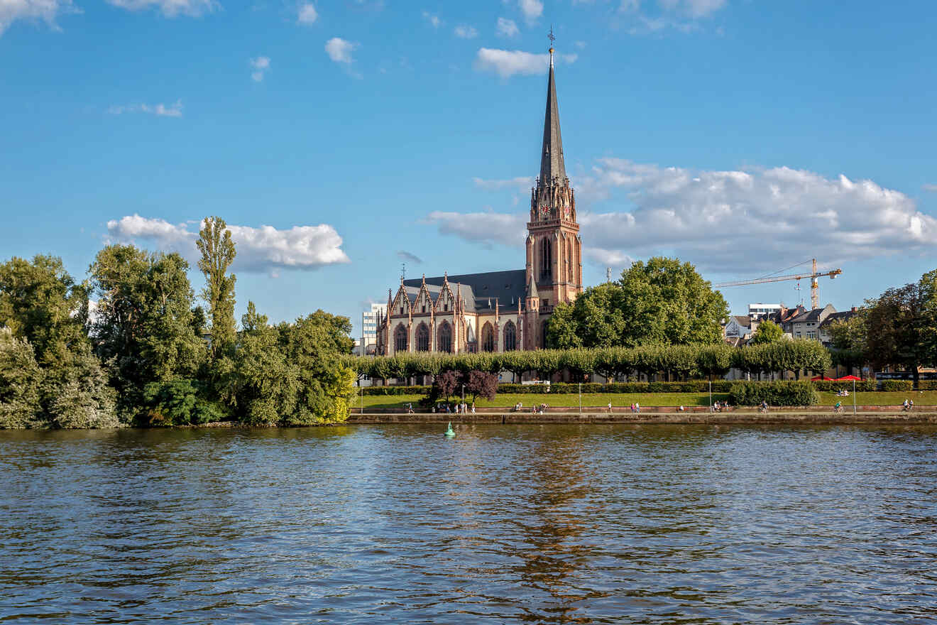 Sunny view of the Main River in Frankfurt, highlighting the Cathedral of Saint Bartholomew with clear blue skies and lush greenery