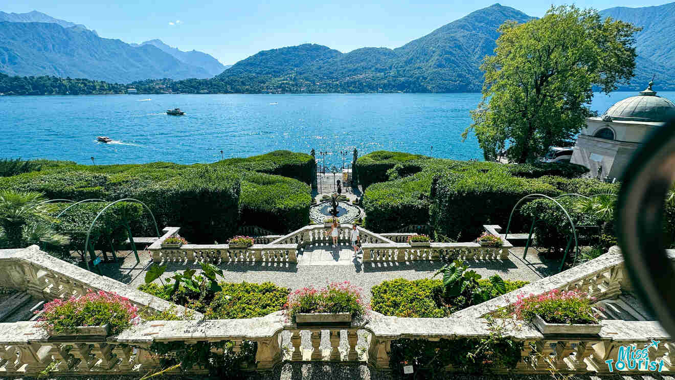 Elegant lakeside garden with symmetrical hedges, a wrought-iron gate opening to Lake Como, and a serene walkway leading to a shaded area