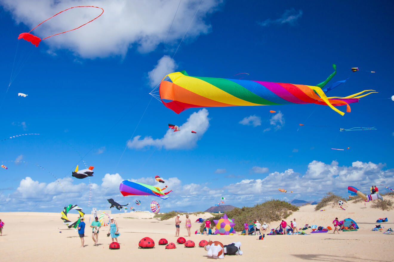 Vibrant kite festival on a Fuerteventura dune, with a blue sky backdrop, featuring an array of colorful kites and spectators enjoying the display