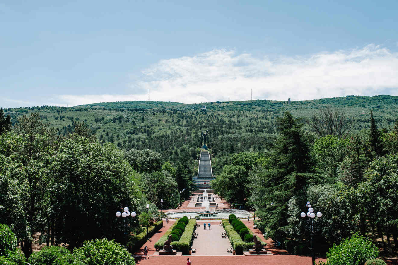 A scenic view of the Vake Park in Tbilisi, with well-manicured hedges and walkways leading to the World War II Memorial of the Eternal Flame.