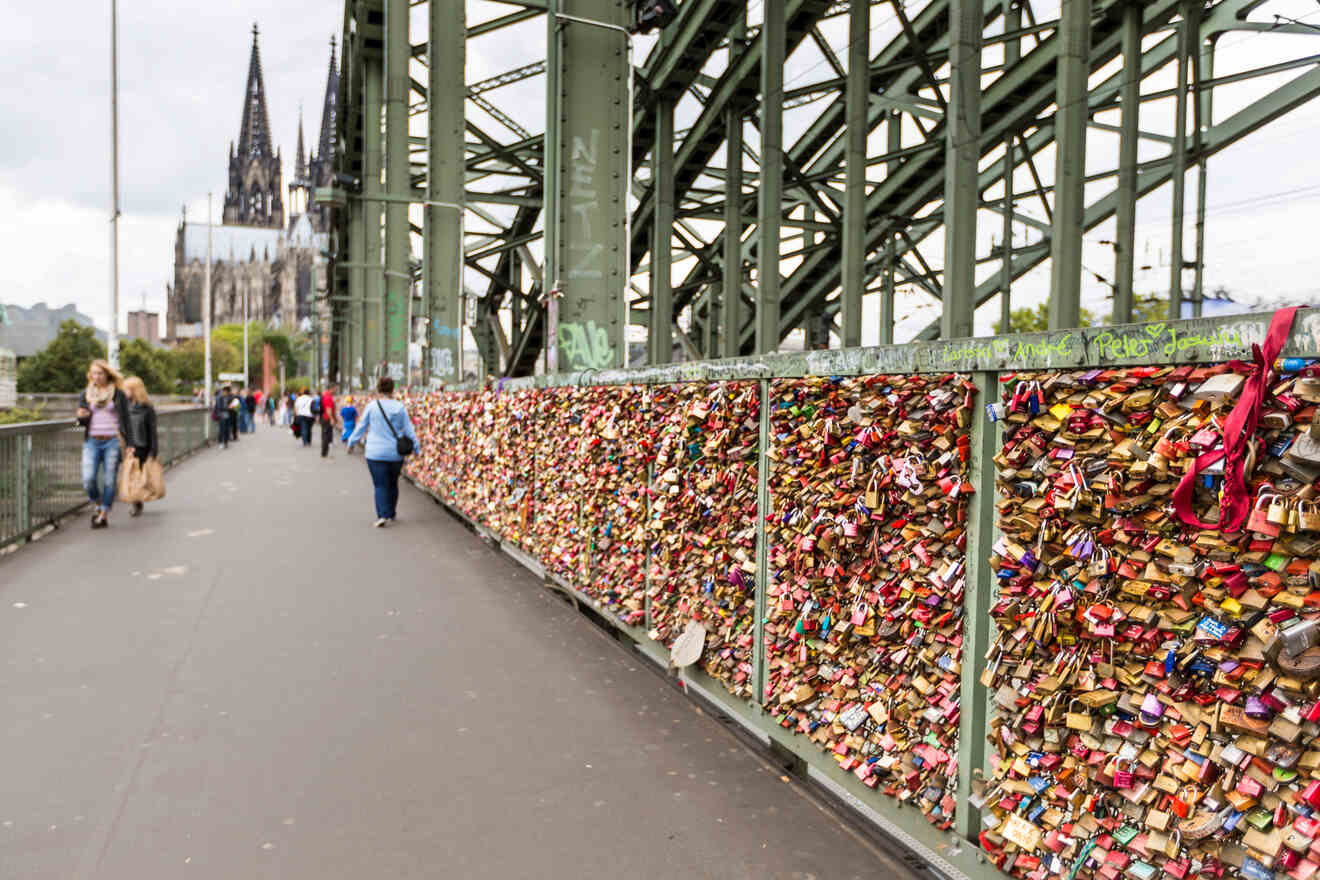 The Hohenzollern Bridge in Cologne, adorned with thousands of colorful love locks, with pedestrians walking alongside.