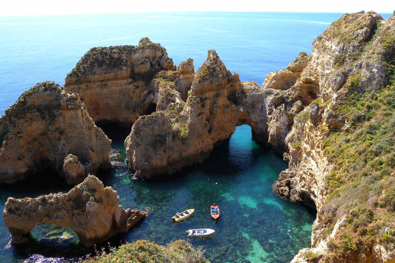 Stunning natural arches and rock formations in clear turquoise waters with small boats floating nearby, as seen from a high vantage point