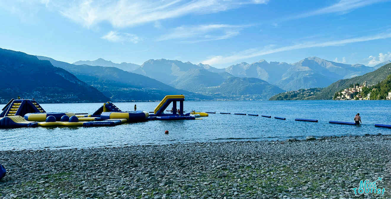 Inflatable water park floating on Lake Como with surrounding mountains, providing a fun and active leisure activity on the pebble beach