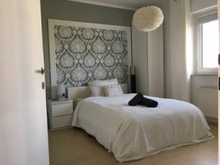 Serene bedroom with a simple white bedspread, patterned headboard, and a fluffy white light fixture, creating a peaceful ambiance