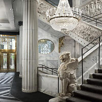Luxurious hotel lobby with a grand marble staircase, elegant chandelier, and a classic statue holding the railing