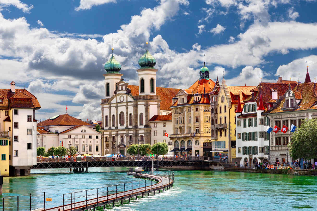 Historic architecture and bustling riverfront in Lucerne, Switzerland, with Jesuit Church dominating the skyline under a dynamic cloud-covered sky.