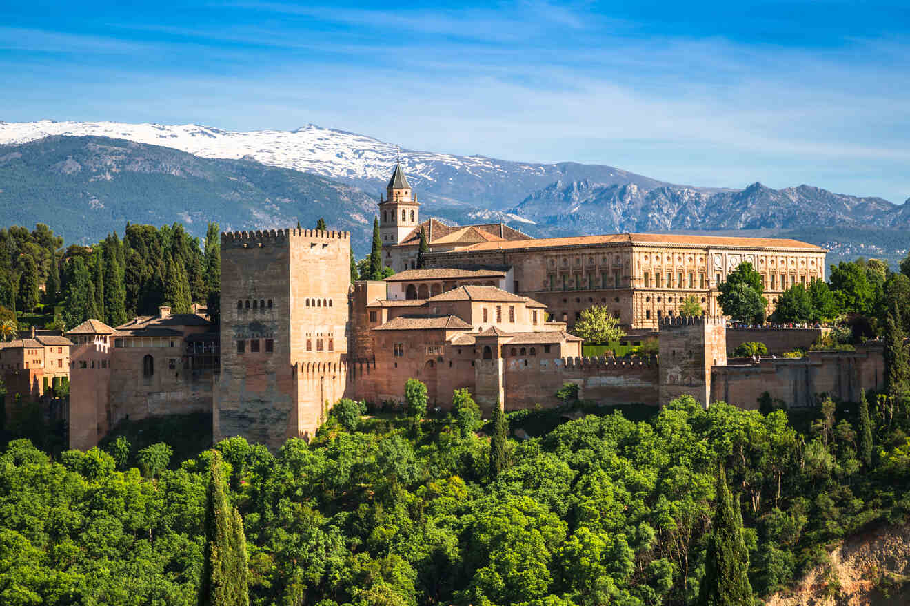 The historic Alhambra Palace in Granada, Spain, stands majestic with its fortified walls and intricate architecture, set against a backdrop of the Sierra Nevada mountains capped with snow