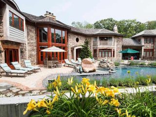 A luxurious stone villa with tall glass windows, complemented by a landscaped pool area with sun loungers and vibrant yellow lilies in the foreground