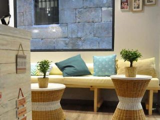 Inviting cafe lounge area with comfortable bench seating, colorful pillows, and wicker stools against a backdrop of a stone wall