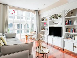 Bright, elegant living room with large windows, a soft gray sofa, and built-in bookshelves, styled with modern decor and a view of city buildings outside