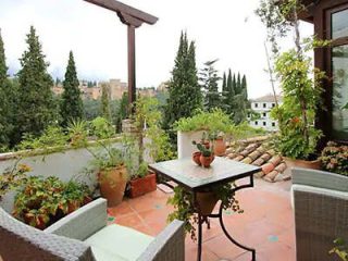 Terracotta-tiled terrace with lush potted plants and comfortable seating, overlooking a historic building surrounded by greenery