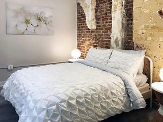 Cozy bedroom with a modern aesthetic, featuring an exposed brick wall, white textured bedding, and a minimalist design