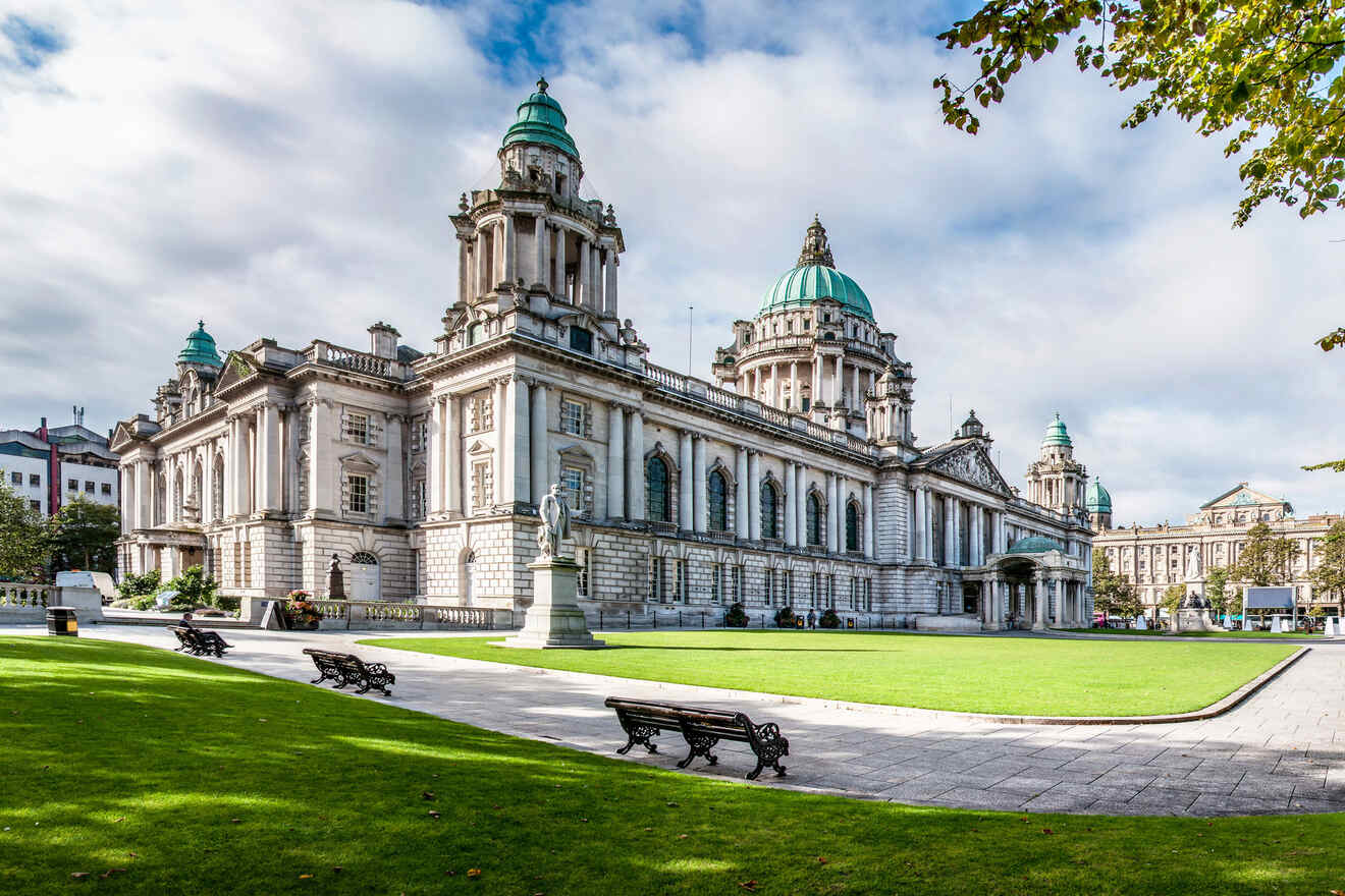 Belfast City Hall standing majestically, its Baroque Revival architecture showcased against a blue sky, with green lawns and benches in the foreground