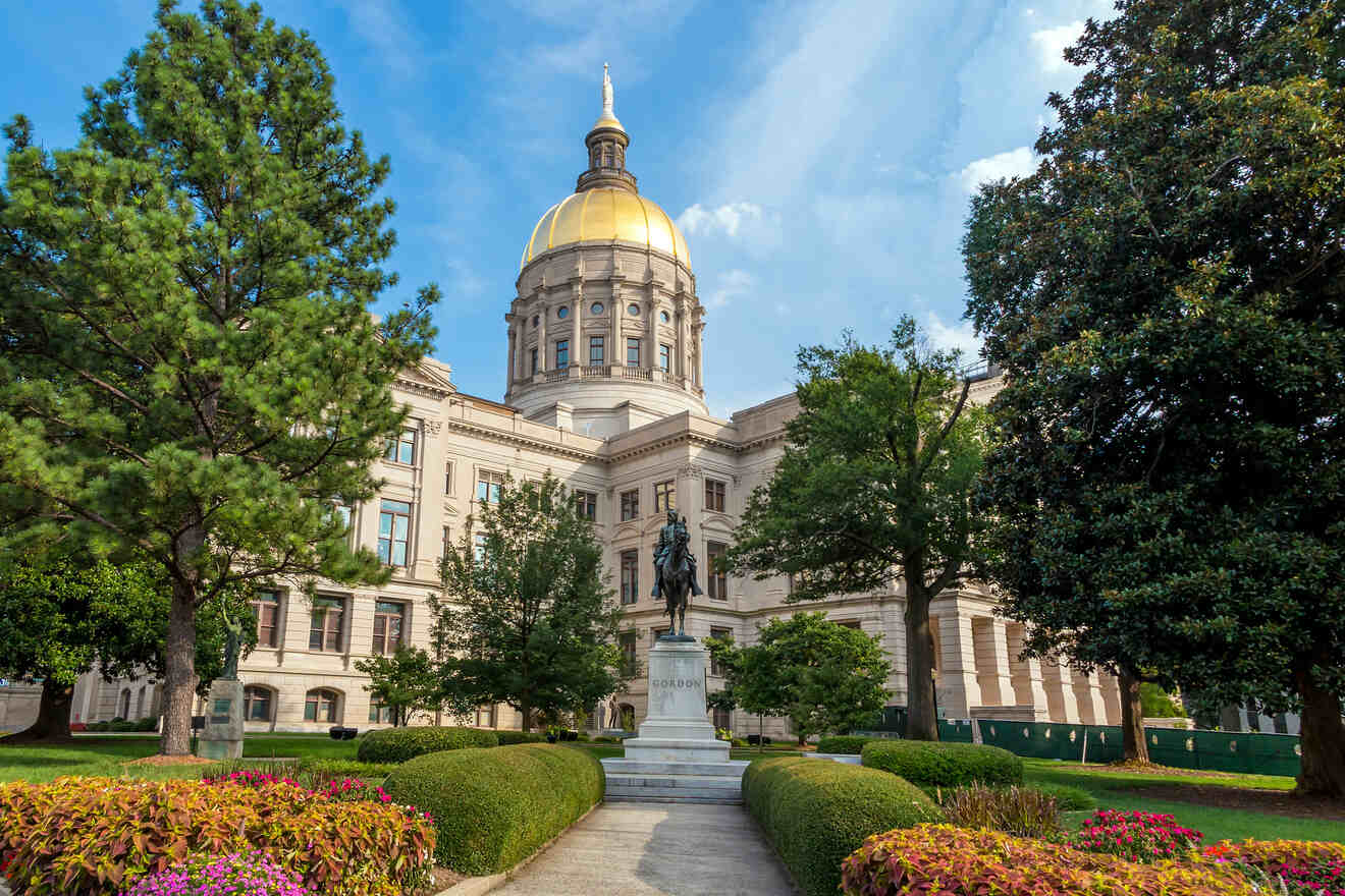 The Georgia State Capitol building in Atlanta, with its prominent gold dome, surrounded by manicured gardens and lush greenery on a sunny day