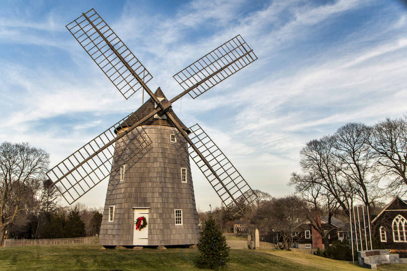 An old-fashioned windmill with four large vanes set against a clear sky, adorned with a wreath on its door, signaling holiday season in a pastoral landscape