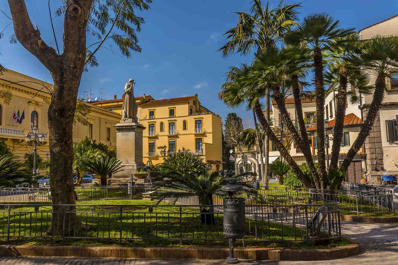 Public square with palm trees, statue, and yellow buildings with European architecture.