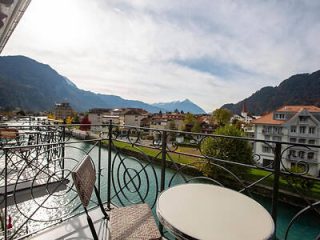 View from a balcony overlooking a picturesque river and traditional Swiss architecture in Interlaken with mountains in the distance
