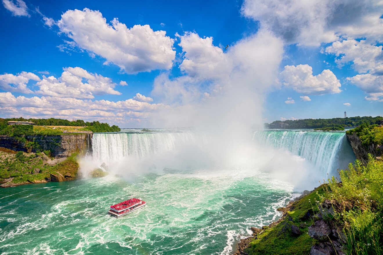 Tourist boat approaching the misty base of Niagara Falls under a blue sky with fluffy clouds.