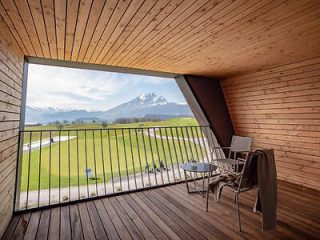 Modern wooden patio with a panoramic view of a mountain landscape, featuring a single chair and a table set against the scenic backdrop