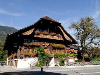 A traditional Swiss chalet adorned with colorful flowers on the balconies, set against a clear blue sky in Interlaken